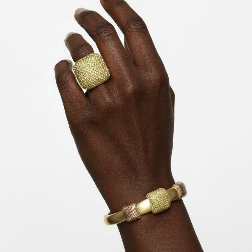 Gold jewelry set including necklace, bracelet, and ring on black mannequin hands with a marble background.
